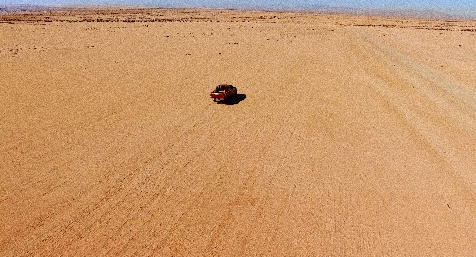 Una camioneta a lo lejos en una extensa planicie del desierto
